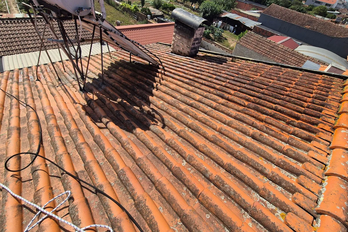Telhado de telha com musgo e depósitos escuros, aquecedor solar e chaminé