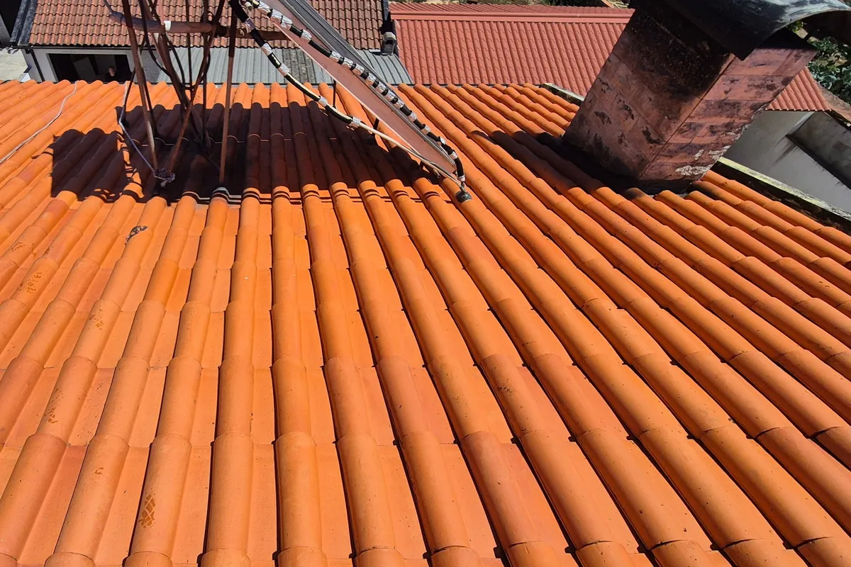 Telhado de telha limpo, de cor laranja uniforme, à volta de um aquecedor solar e de uma chaminé
