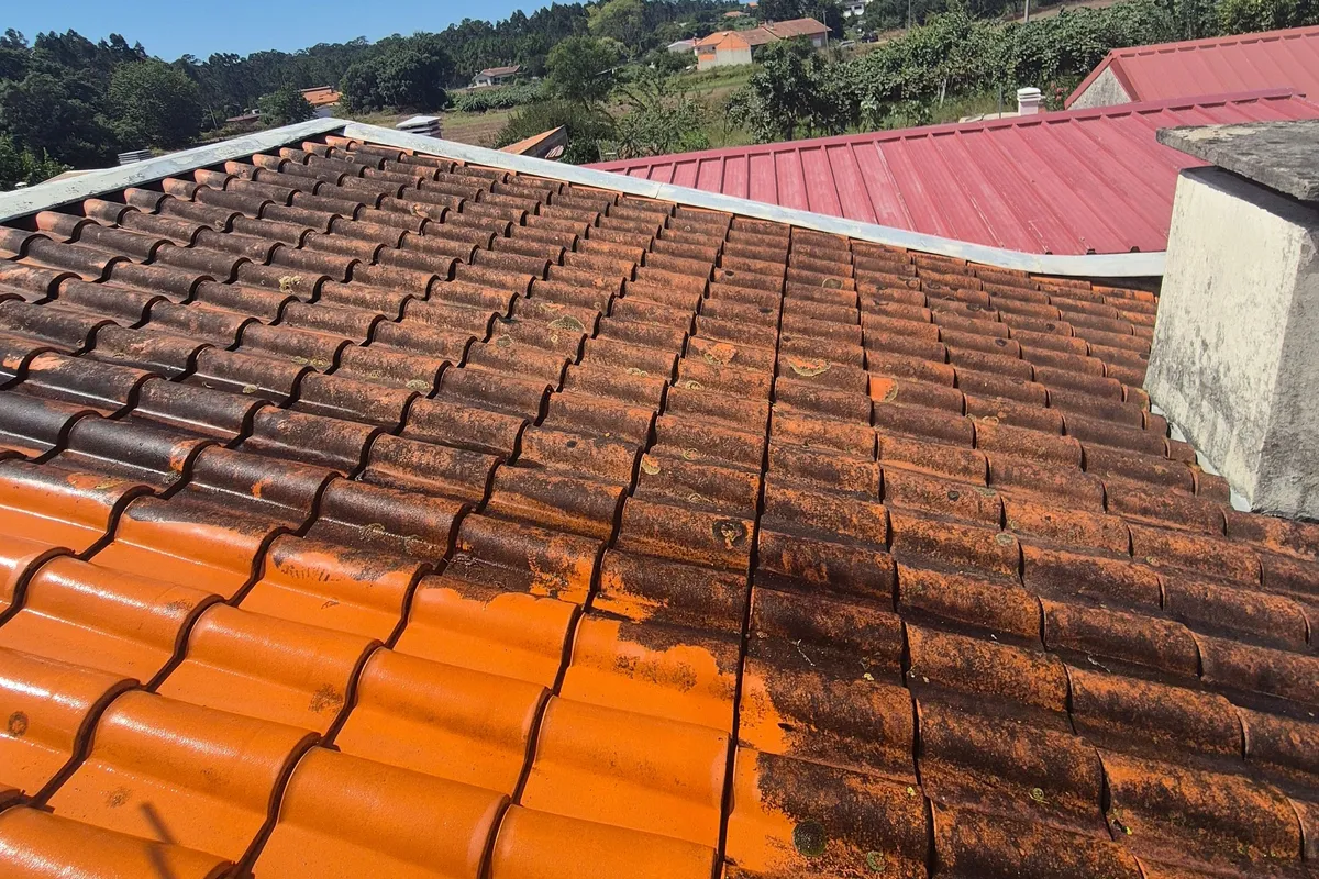 Telhado de telha em limpeza, algumas faixas laranja em primeiro plano, telhas escuras até à cumeeira, chaminé à direita